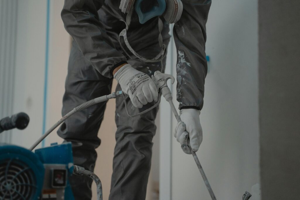 Worker in protective gear using a power spray for indoor renovation.